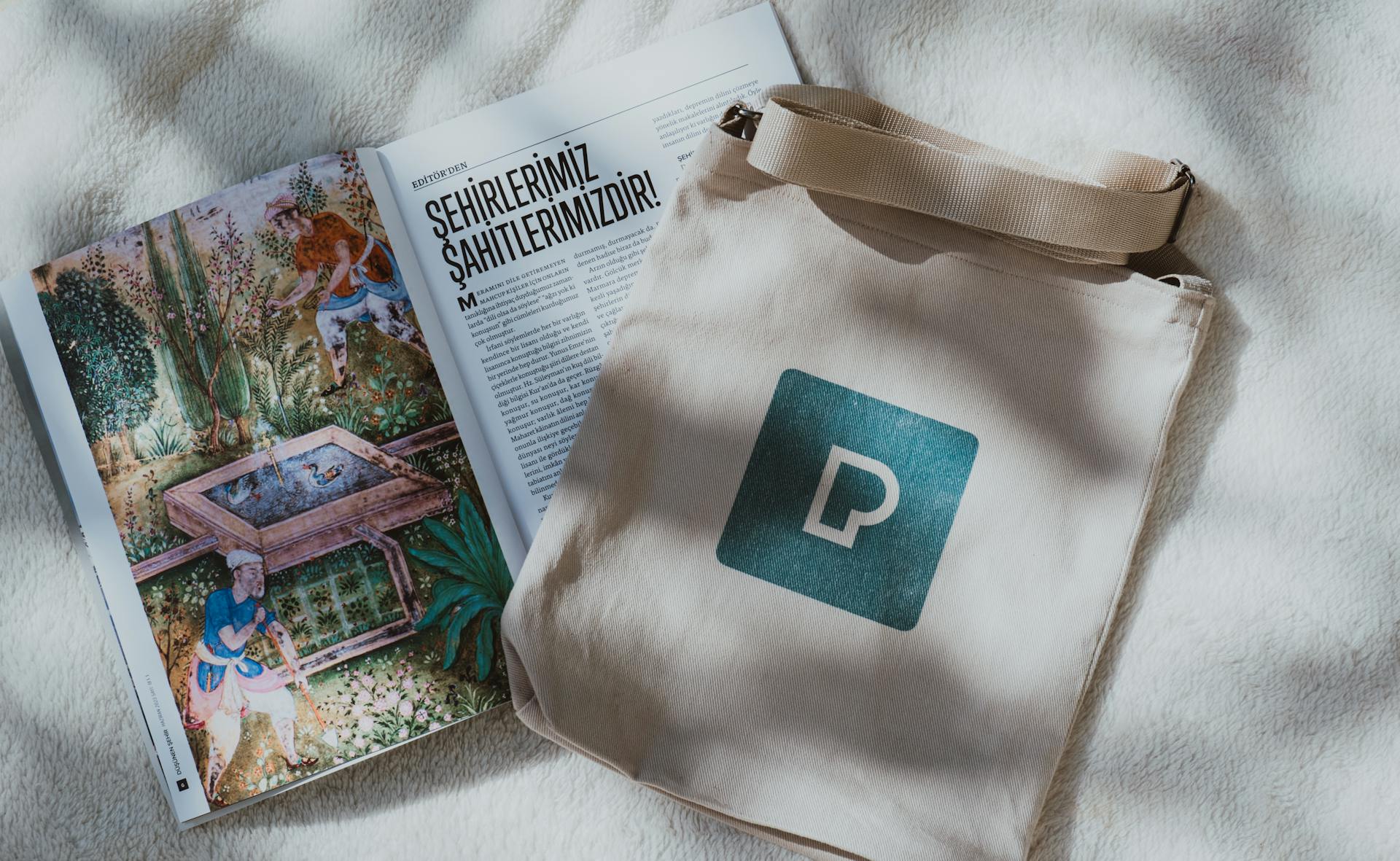 Open illustrated magazine with canvas tote bag on a soft fabric surface, displaying text in Turkish.