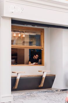Man working on a laptop by a cafe window, offering a cozy and focused workspace vibe.