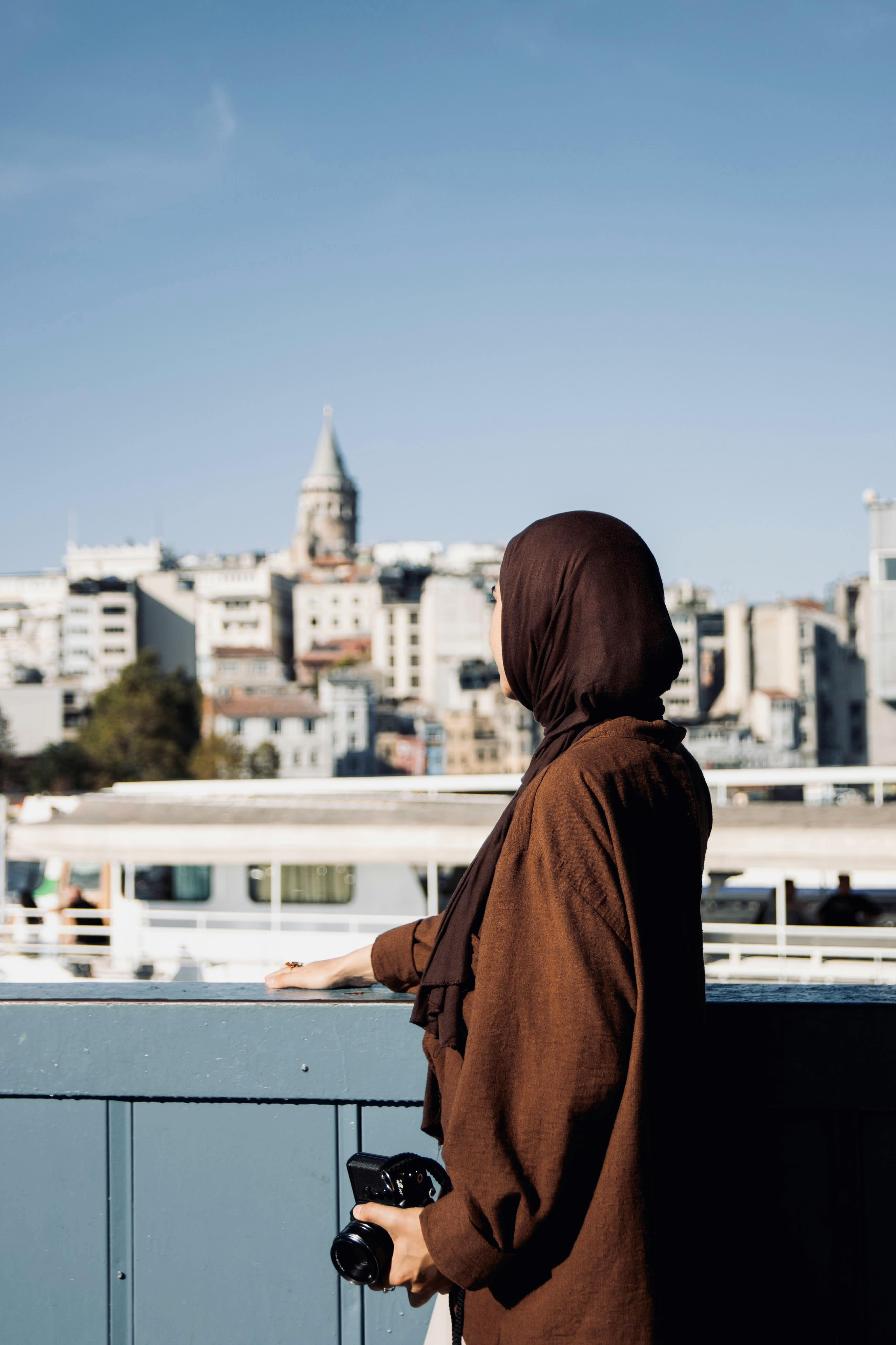A woman with a headscarf admires a cityscape with a skyline in the background.