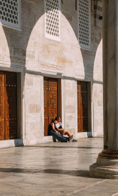 Free A serene moment captured of a couple sitting against wooden doors, bathed in afternoon sunlight. Stock Photo