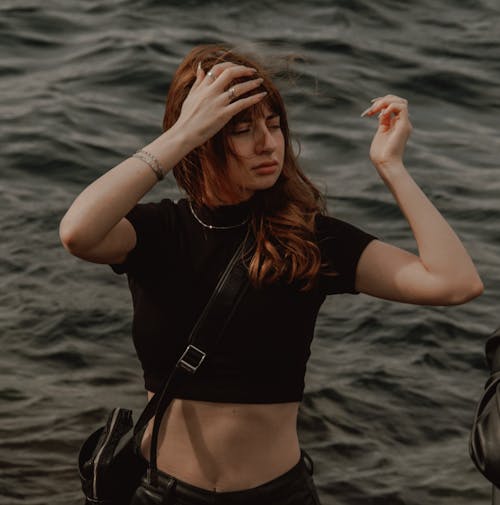 Woman in Black Crop Top Fixing Hair by a Sea