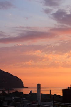 Beautiful coastal sunset with pink and orange skies reflecting on the ocean, creating a serene silhouette scene.