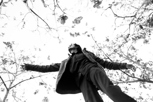 A striking black and white image of a man reaching towards treetops with a dramatic angle.