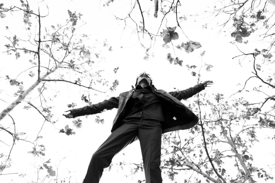 Black and white image of a man standing under trees, arms spread wide, emphasizing freedom.