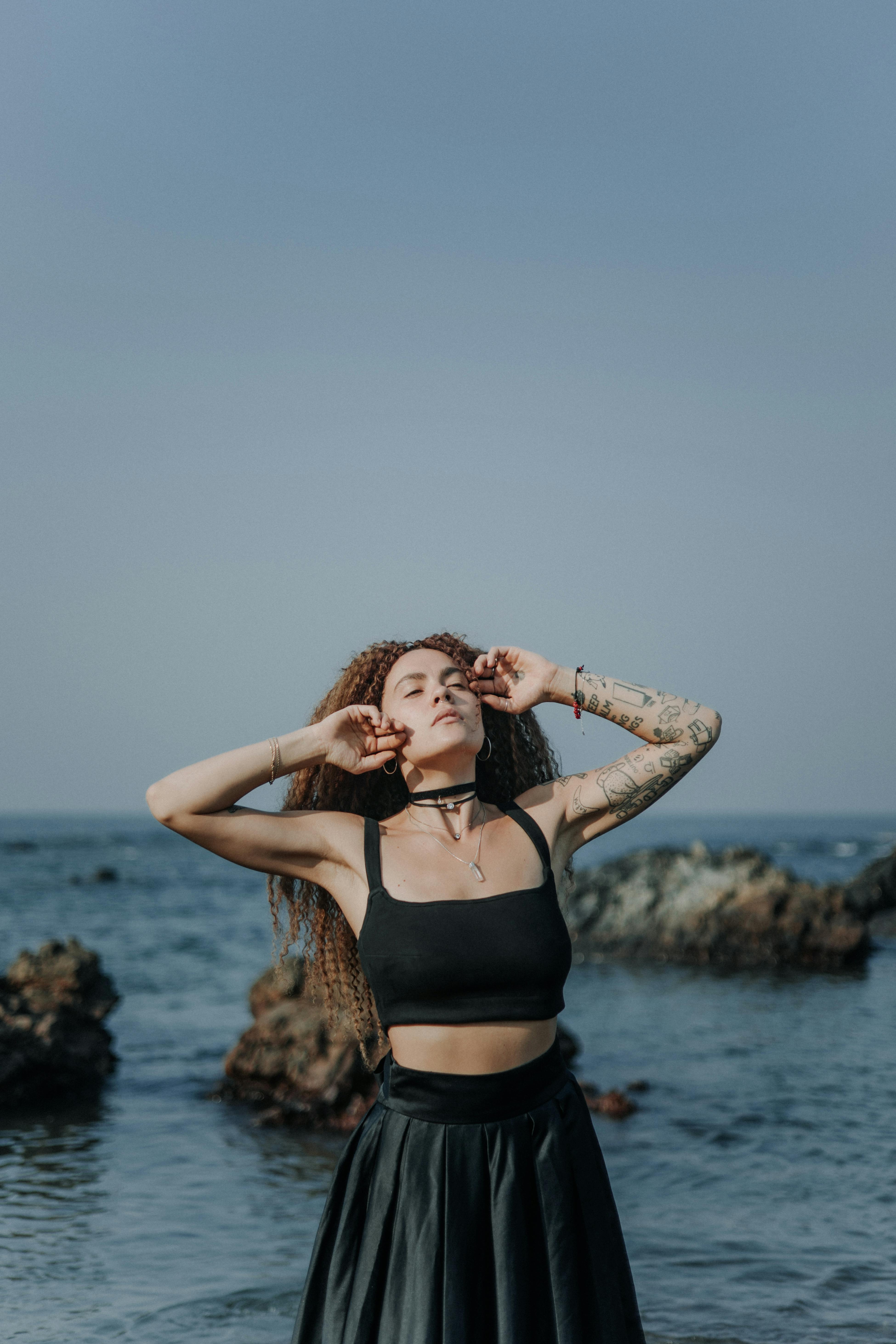 身着黑色连衣裙的时尚女子在海边优雅地摆姿势，散发着自信与魅力