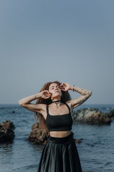 Stylish woman in black dress poses by the ocean, exuding confidence and elegance.