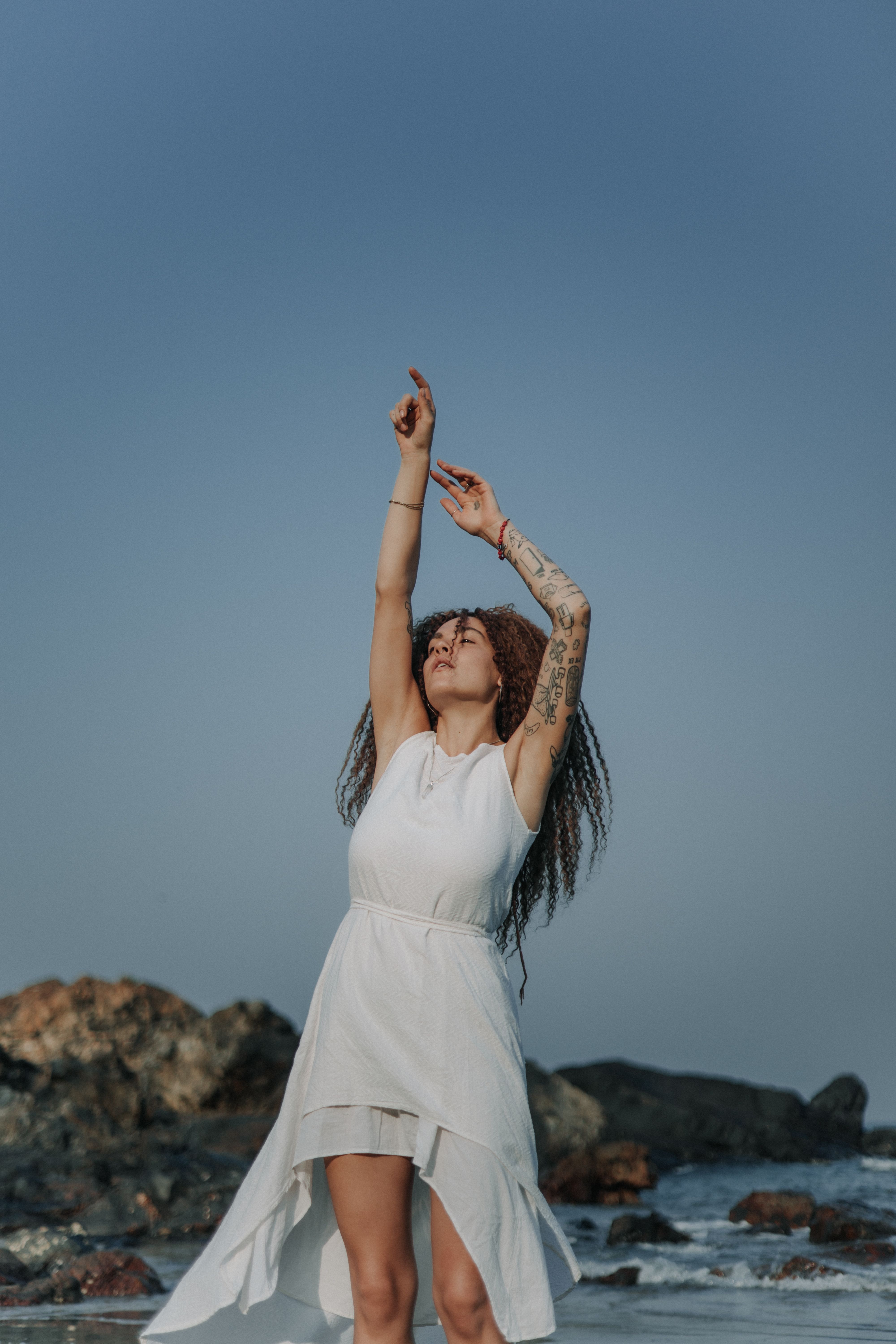 Woman in White Dress Standing with Raised Arms on Beach · Free Stock Photo