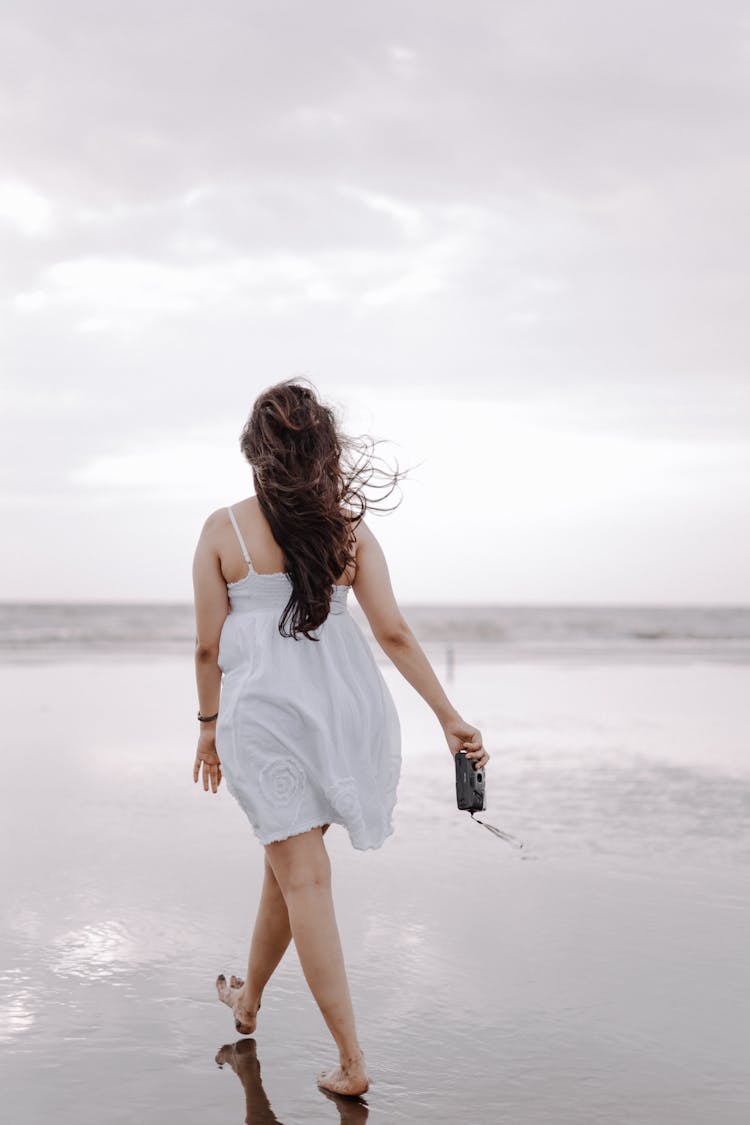 Woman Walking On A Beach With A Camera 