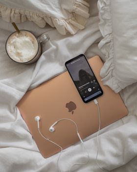 A cozy setup featuring a laptop, coffee, and smartphone on a ruffled bed cover.