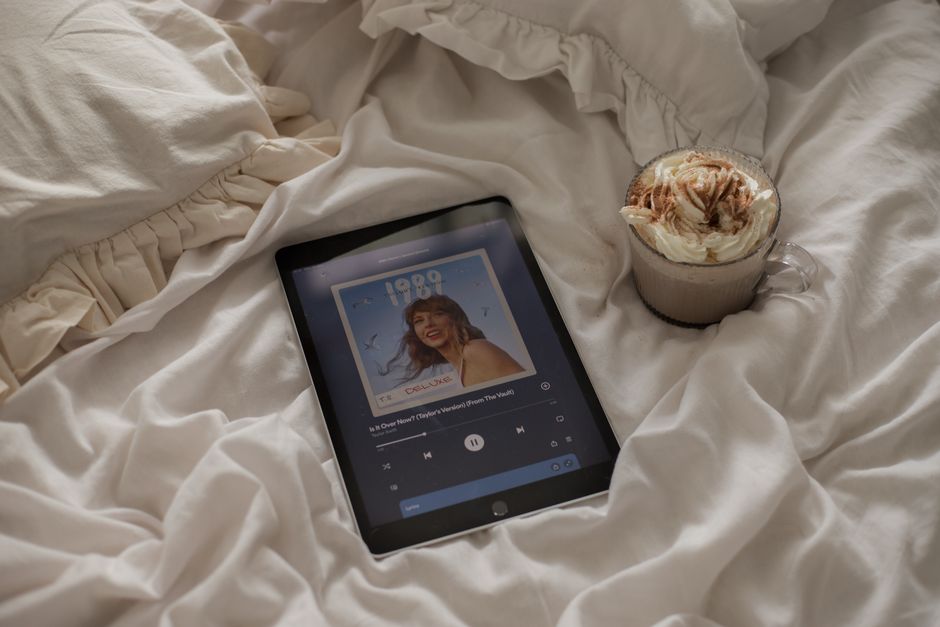 Serene morning scene with a tablet playing music and a coffee on a rumpled bed.