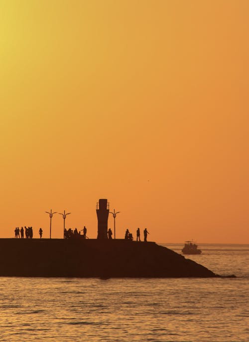 People around Lighthouse on Sea Coast under Clear, Yellow Sky