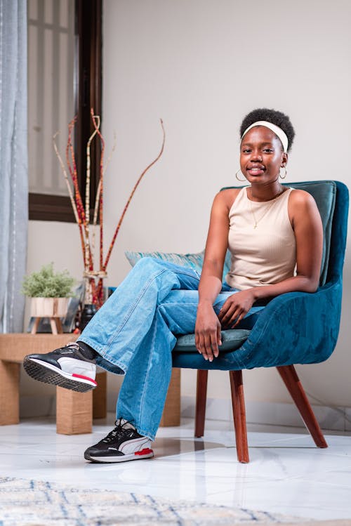 Woman in Beige Top and Blue Jeans Sitting in a Blue Armchair