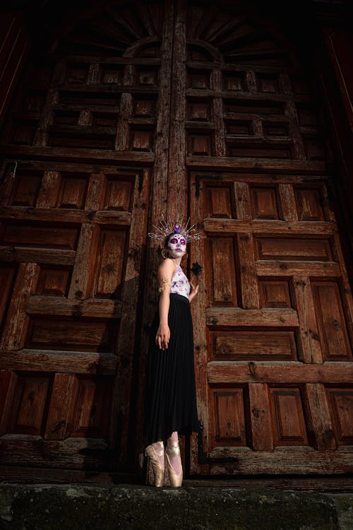 Low Angle Shot of a Woman Dressed as a Catrina Standing in front of Wooden Door 