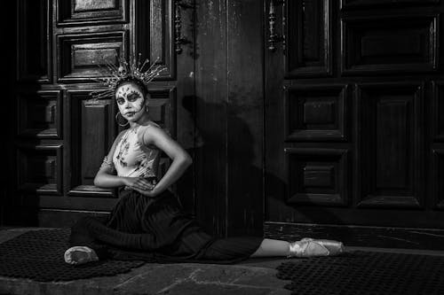 Black and White Photo of a Woman Dressed as a Catrina Sitting in front of the Door 