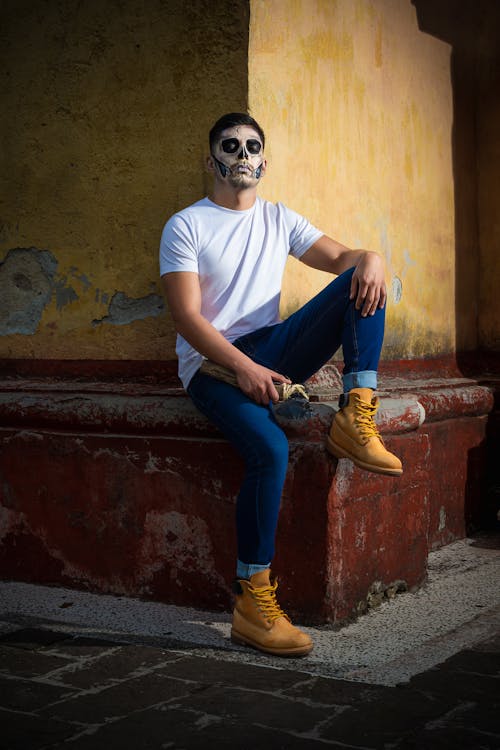 Man in Sugar Skull Makeup Sitting on the Corner of a Building 