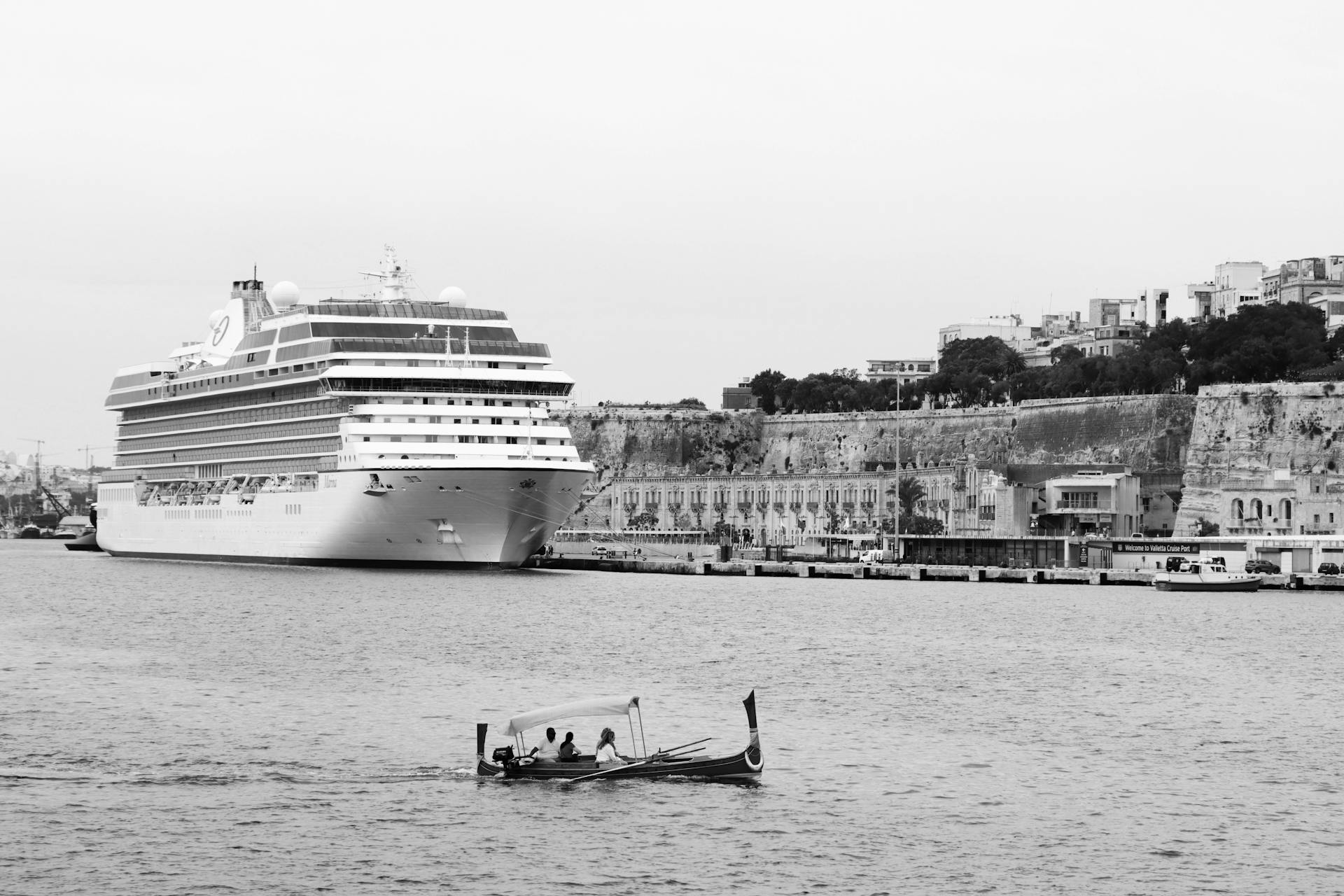 Monochrome image of a cruise ship docked in Valletta Harbor, showcasing Maltese architecture.