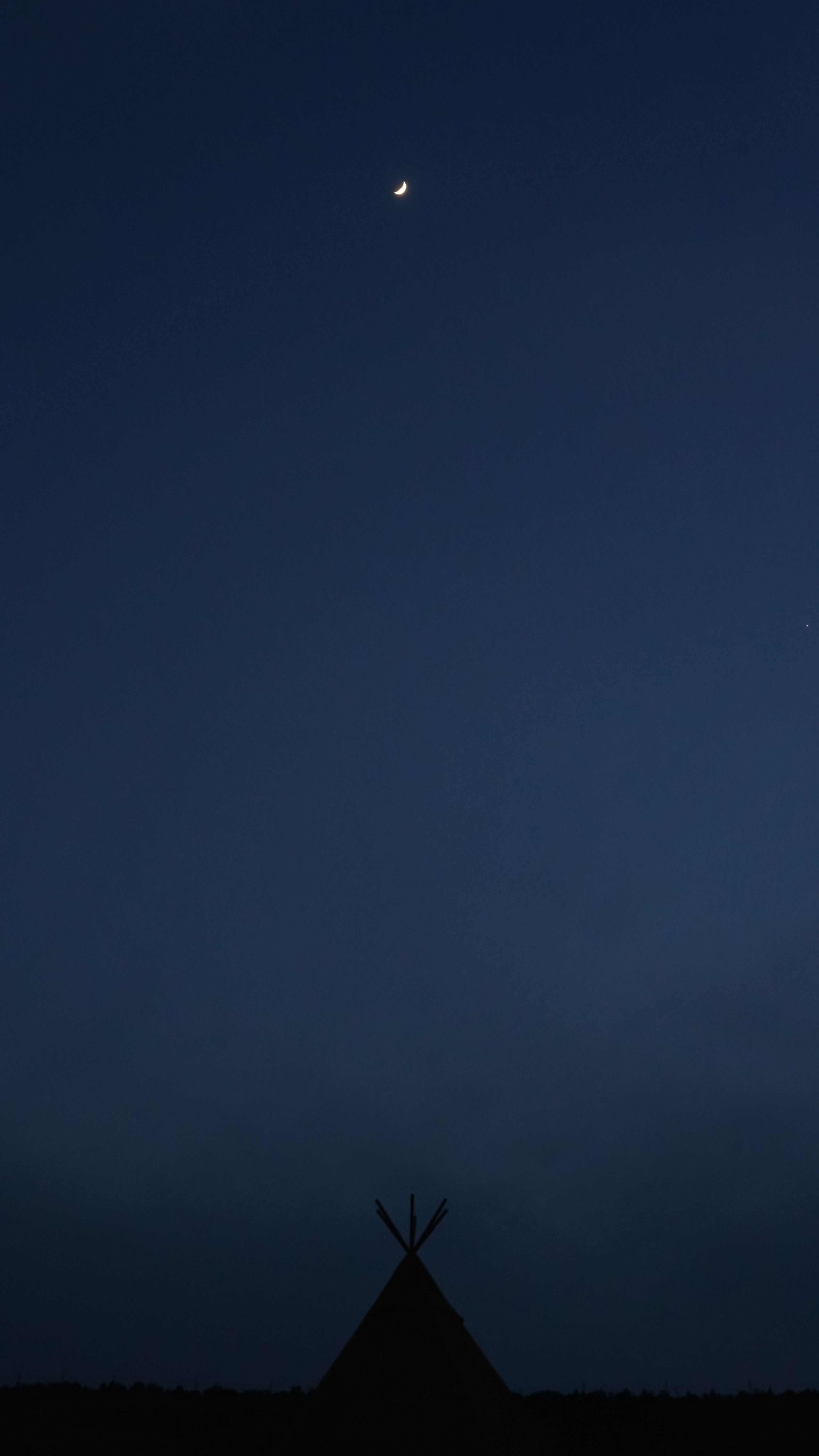 A serene crescent moon over a silhouetted tent at night against a clear sky.