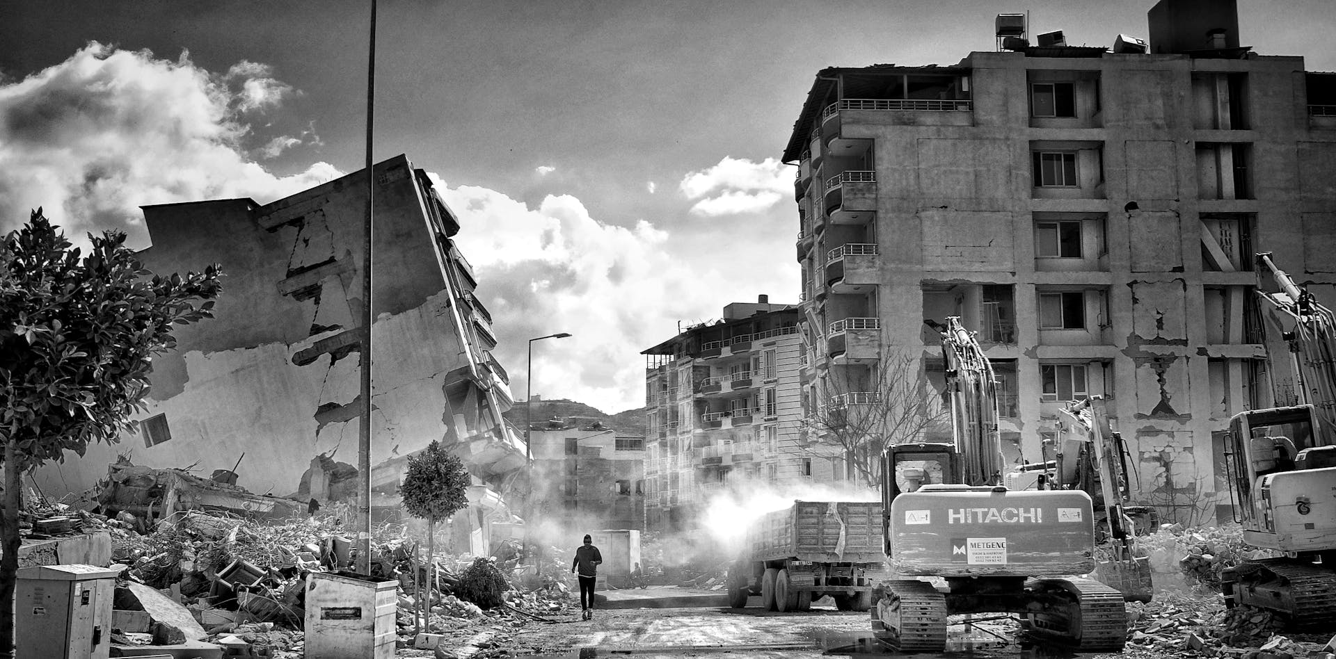 Excavators Clearing Rubble from a City Street with Collapsed Houses