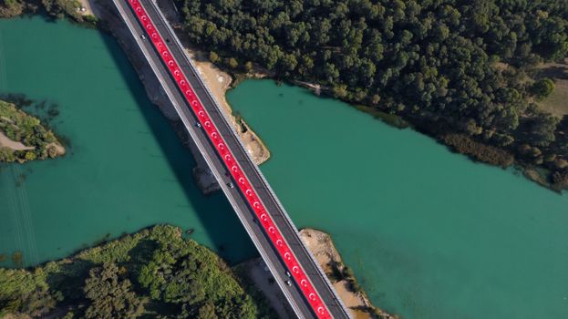 Drone shot capturing the vibrant Seyhan River and bridge in Adana, Türkiye, adorned with Turkish flags.