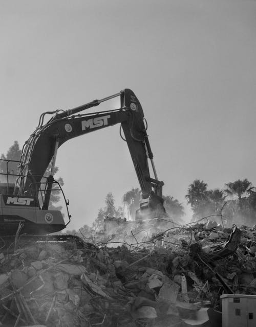 Black and White Photo of an Excavator Working on a Pile of Rubble