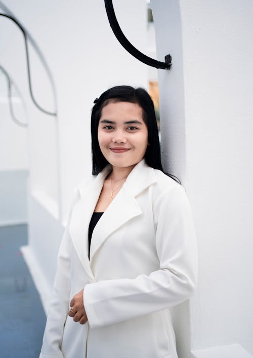 Young Elegant Woman in a White Blazer Standing by a White Wall 