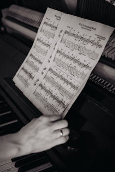 A black and white photo of a hand adjusting sheet music on a piano.