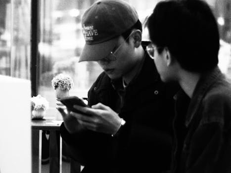 Two men in casual attire engaged with smartphones in a black and white indoor urban setting.
