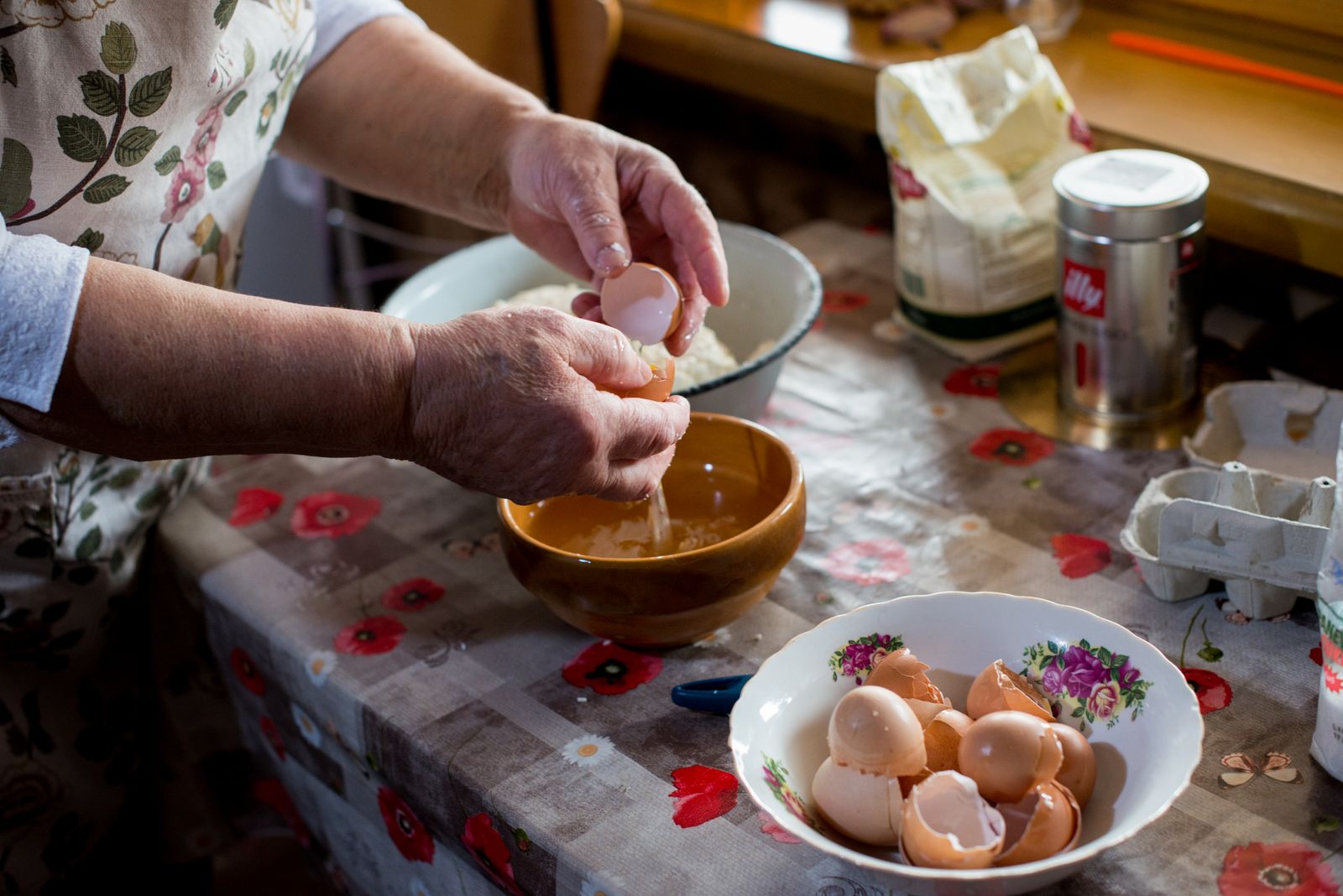 Senior woman cracking eggs into a bowl for cooking in a cozy kitchen setting.