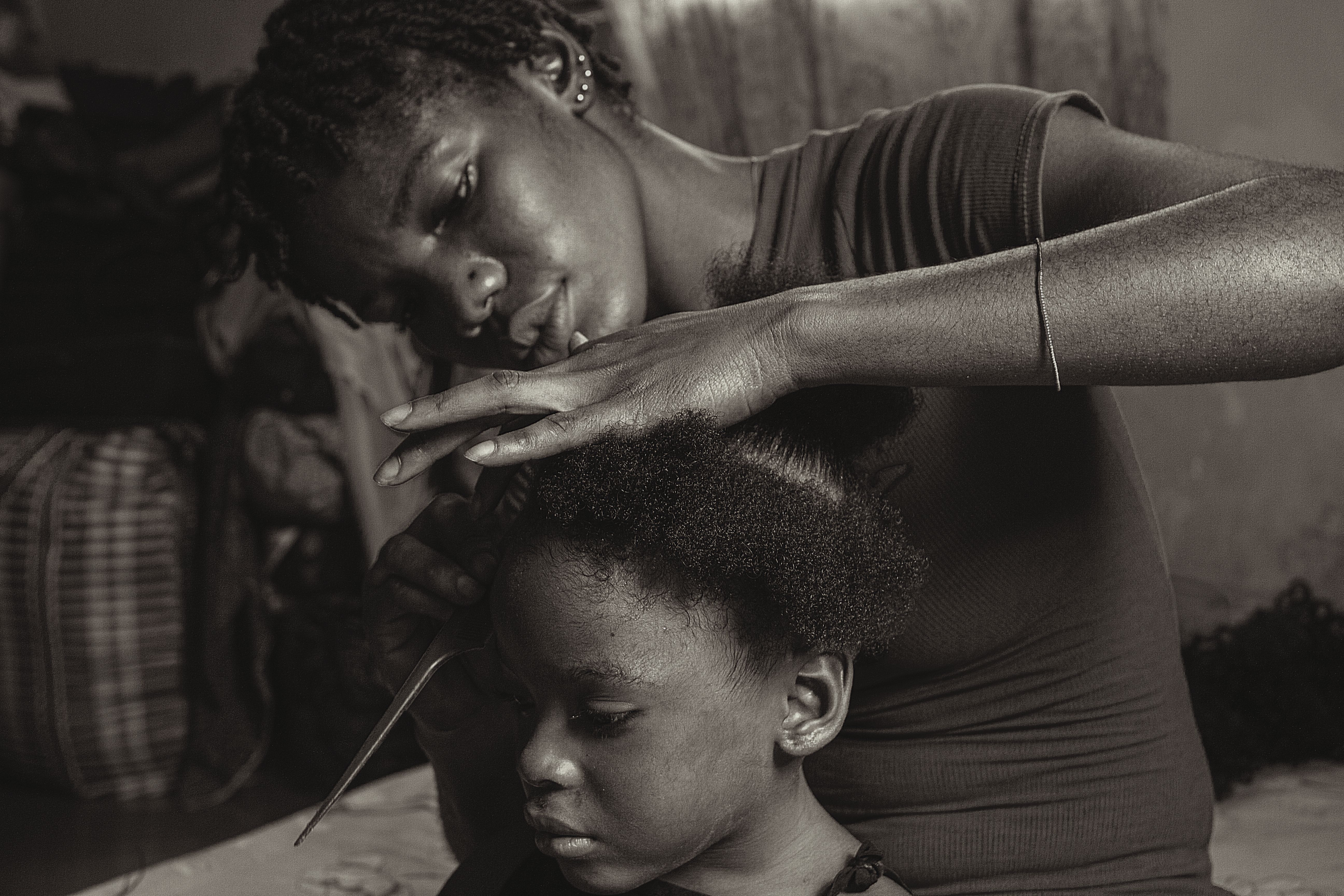 A touching scene of a woman carefully styling a young girl's hair indoors in black and white.