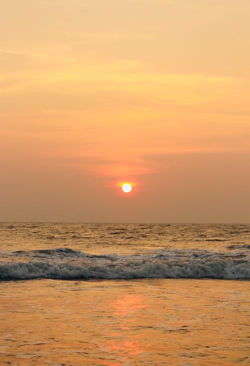 Free A serene sunset over the ocean with gentle waves and a warm orange sky. Stock Photo