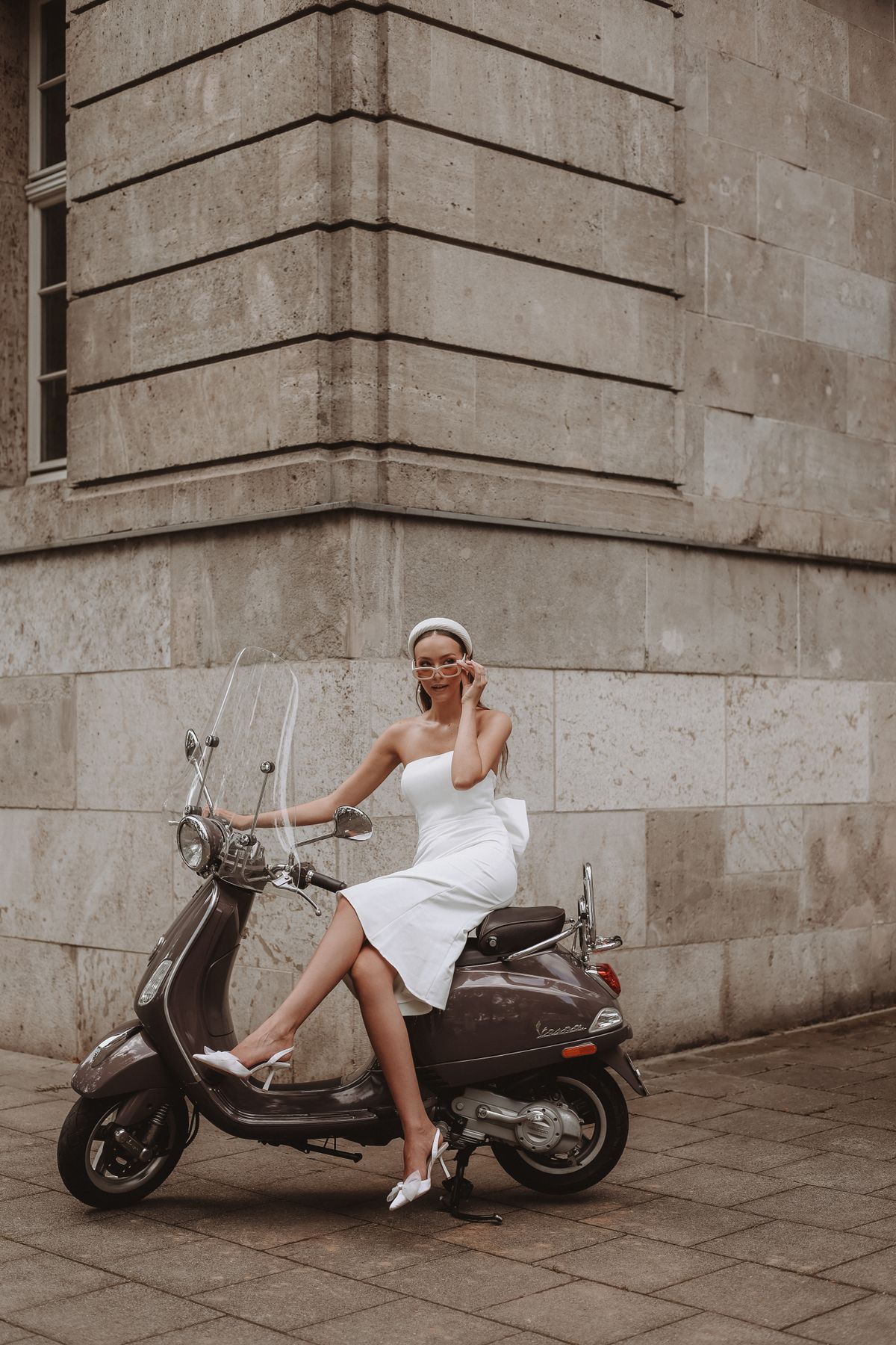 Model in a white midi off-the-shoulder dress on a Vespa