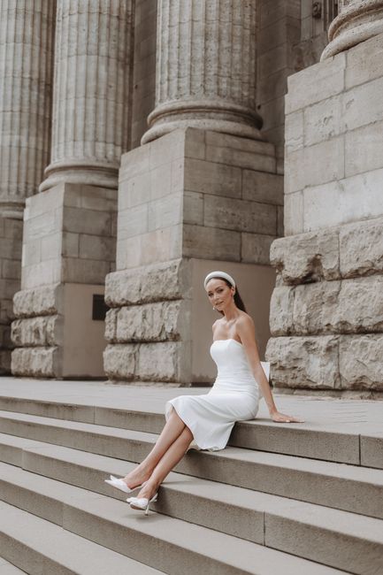 A stylish bride in a white dress poses on steps next to a historic colonnade in Cologne, Germany.