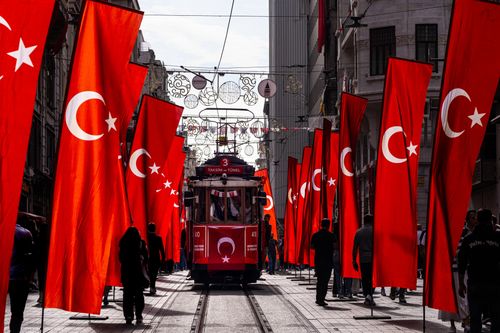 Free A classic red tram surrounded by Turkish flags in Istanbul, Türkiye, on a bustling city street. Stock Photo