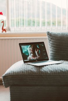 Cozy home workspace setup with a laptop on a textured grey sofa near bright windows.
