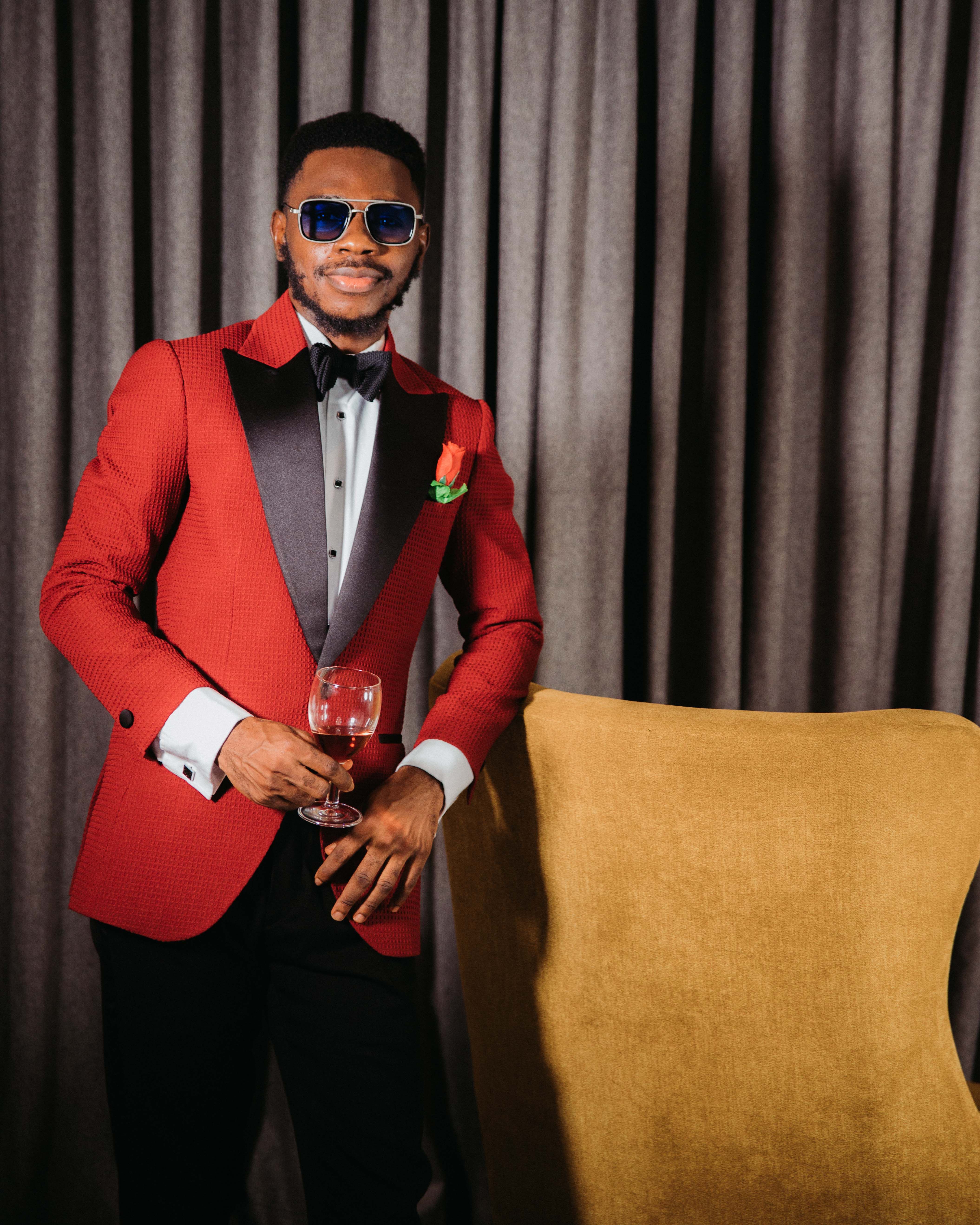 Stylish man in a red suit holding a wine glass, standing confidently indoors.