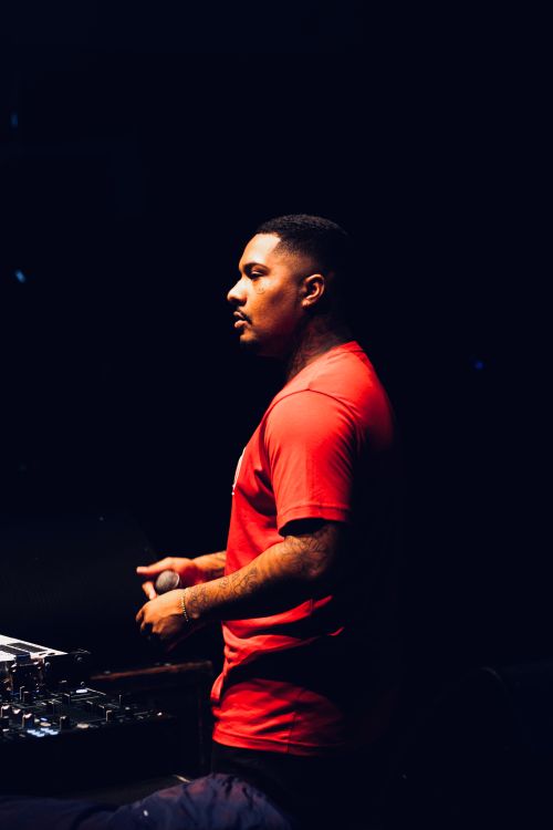 Free A DJ in a red t-shirt stands by a sound mixer, engaging a crowd on stage. Stock Photo