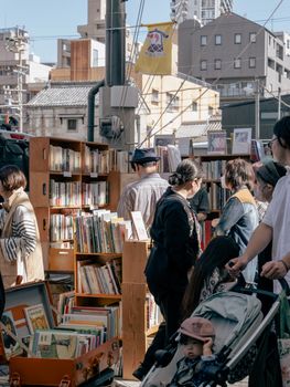 Outdoor book market in Nagoya, Japan with people browsing shelves filled with books on a sunny day.