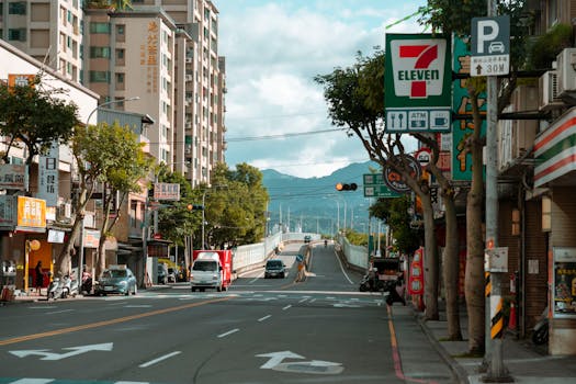 City street scene featuring a 7 Eleven store, cars, and urban buildings with mountains in the background.