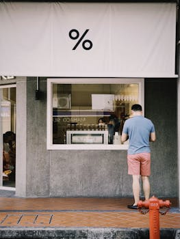A man stands casually outside a coffee shop with a modern design on a city street.