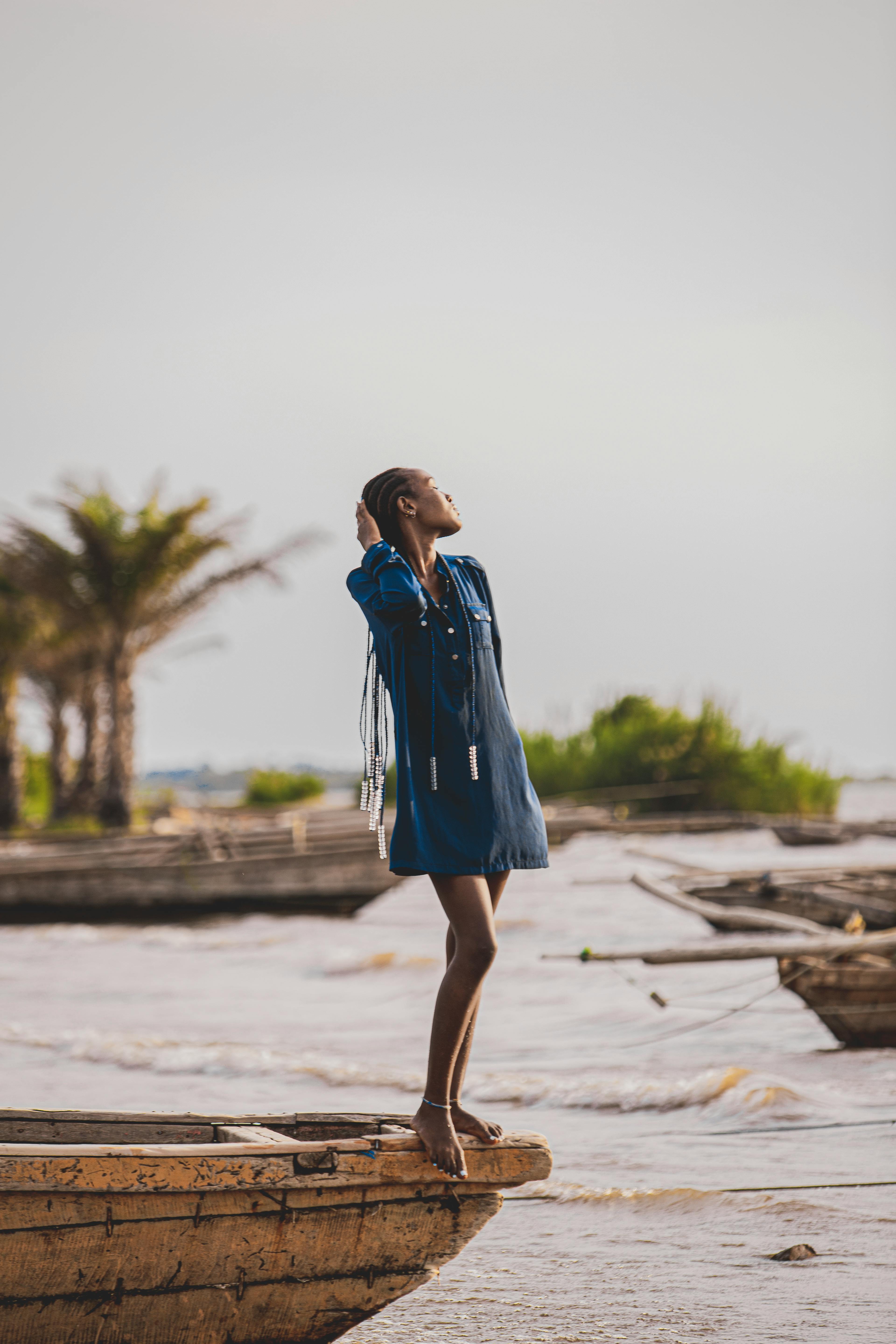 Black woman in stylish outfit standing on a wooden boat by the lakeshore, showcasing elegance and confidence.