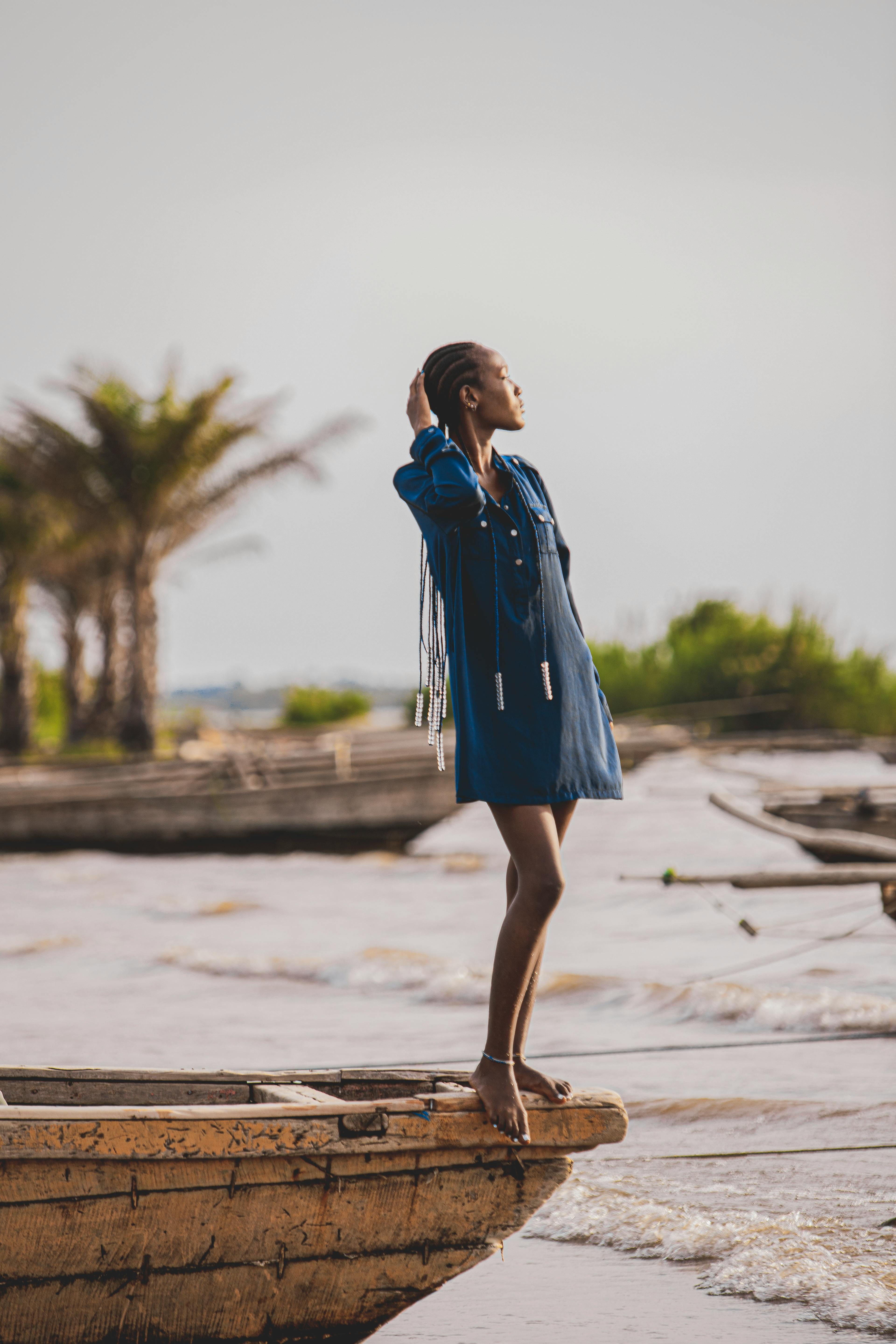 Stylish woman standing on a wooden boat along a serene lakeshore, showcasing modern fashion in a natural setting.