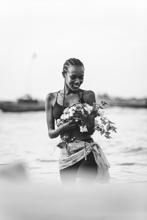 Free Black and white photo of a smiling woman holding flowers by the water. Stock Photo