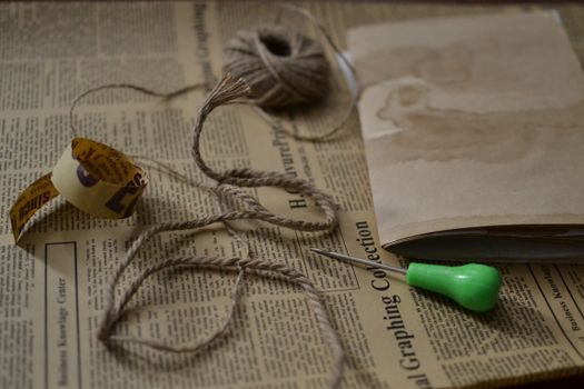 A close-up of vintage crafting tools including thread, paper, and a screwdriver on a newspaper.