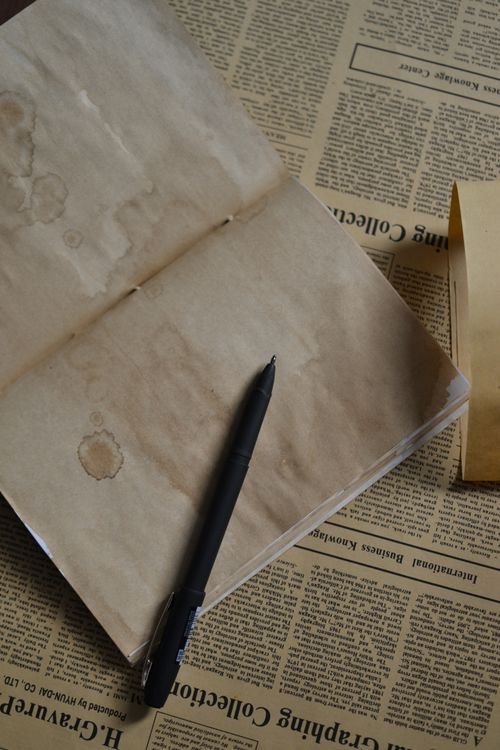 Free A vintage notebook with a pen resting on aged newspaper pages, captured from above. Stock Photo