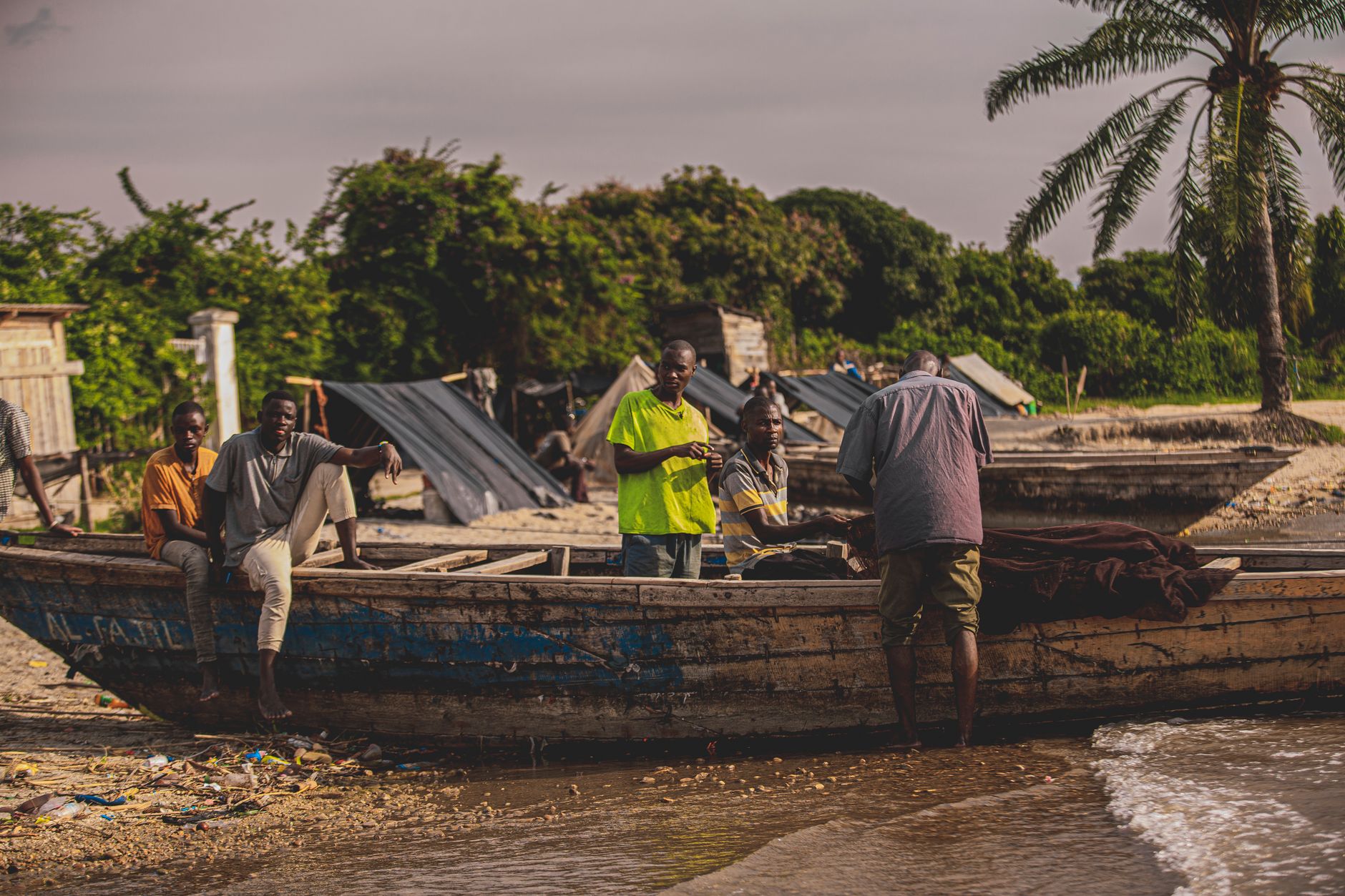 Men working on a wooden fishing boat at a rural tropical beach village.