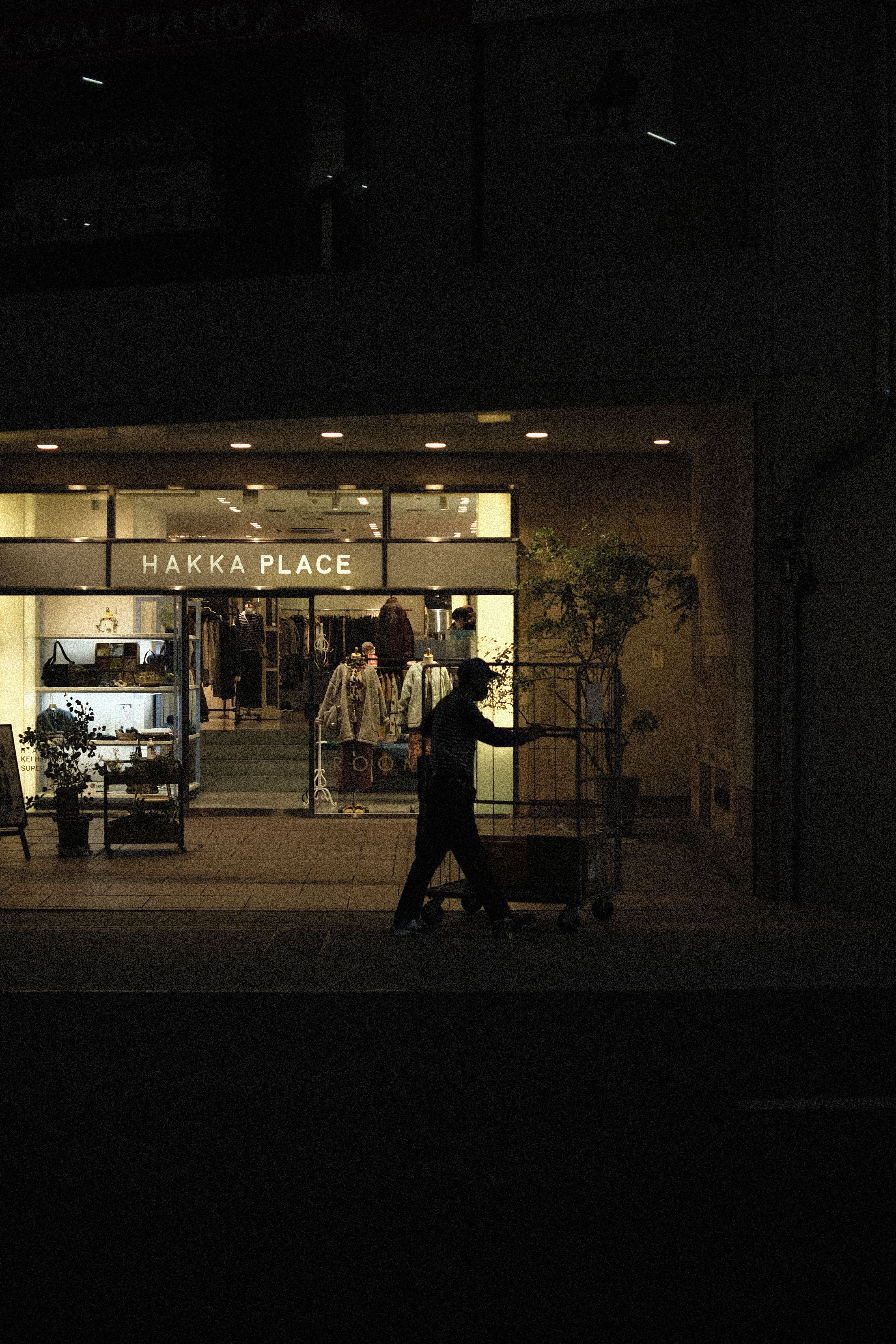 Silhouette of a person walking by a stylish clothing store at night.