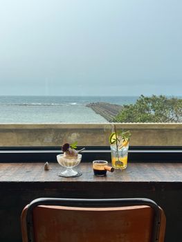 Serene seaside view through window with drinks and dessert on table.