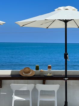 Serene ocean view with beach umbrella, chairs, and refreshing drinks.