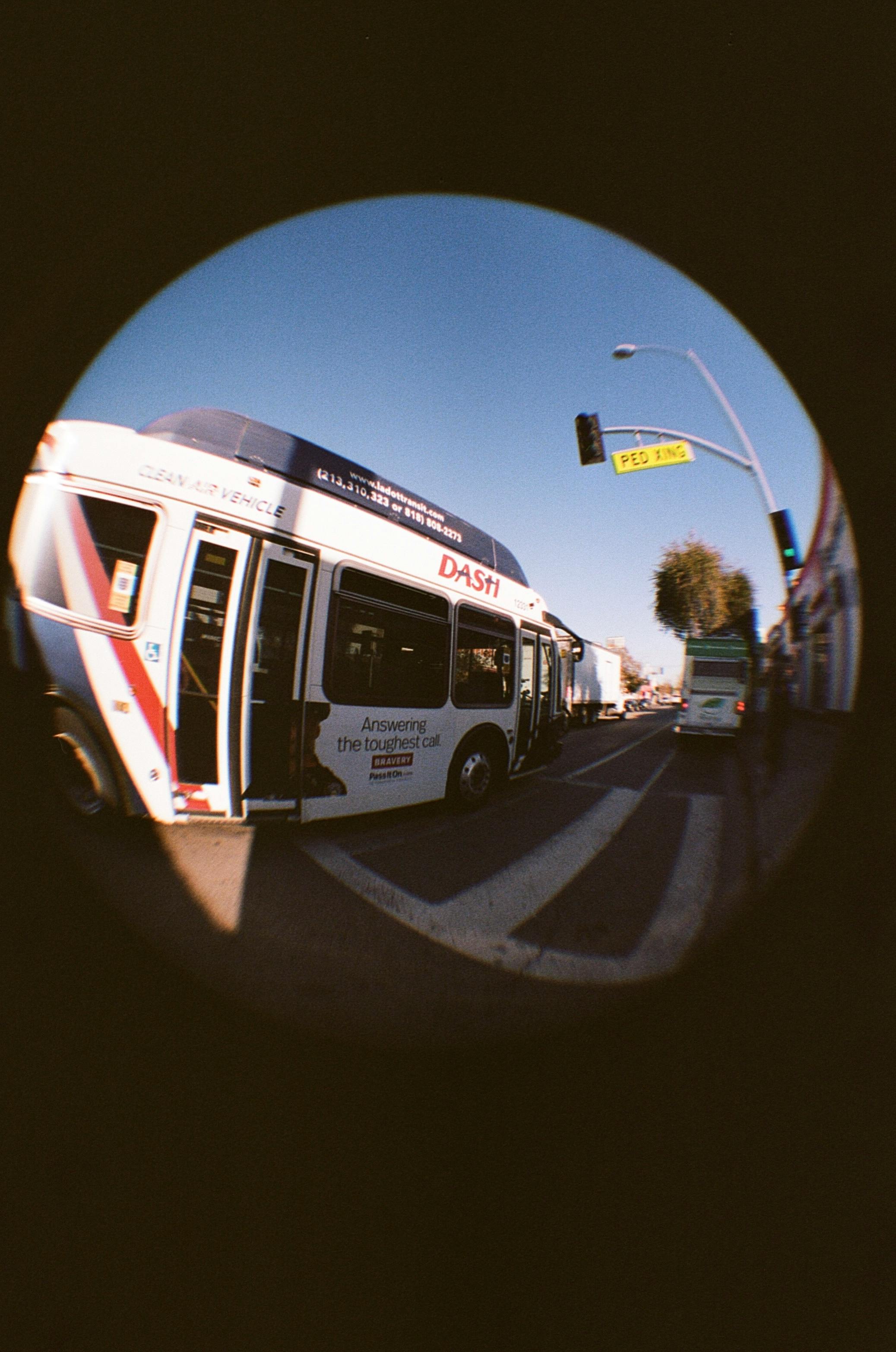 Street view featuring a city bus in motion captured with a fisheye lens, showcasing urban life.