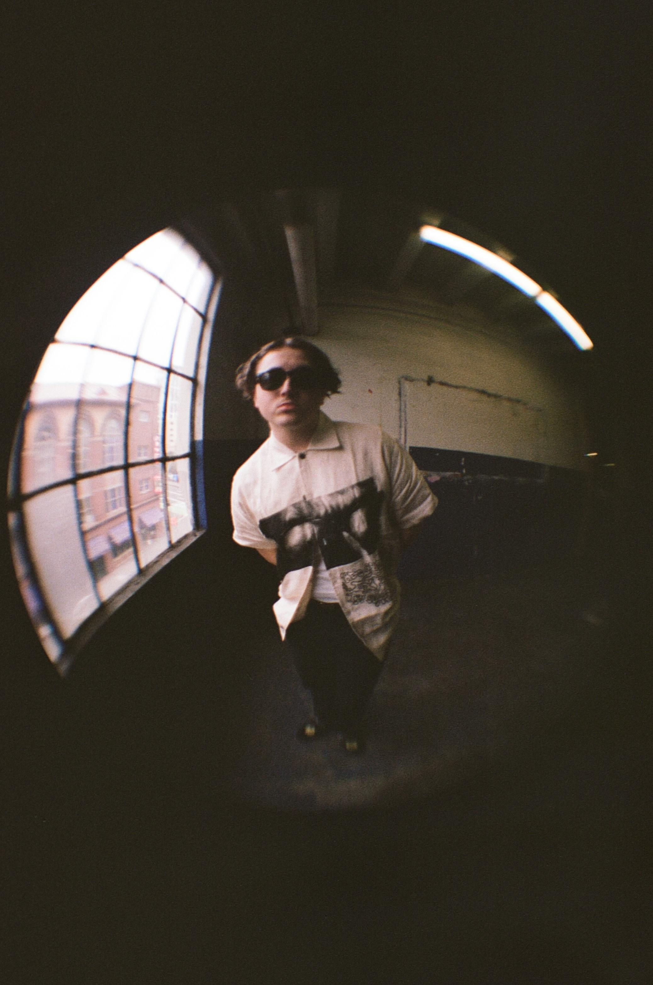 Artistic fisheye lens photo of a man standing indoors wearing sunglasses, featuring a distorted perspective.